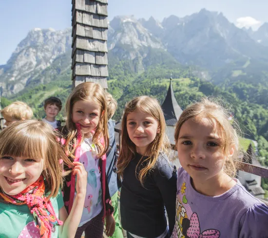 Group of smiling children on a scenic balcony with alpine mountains in the background