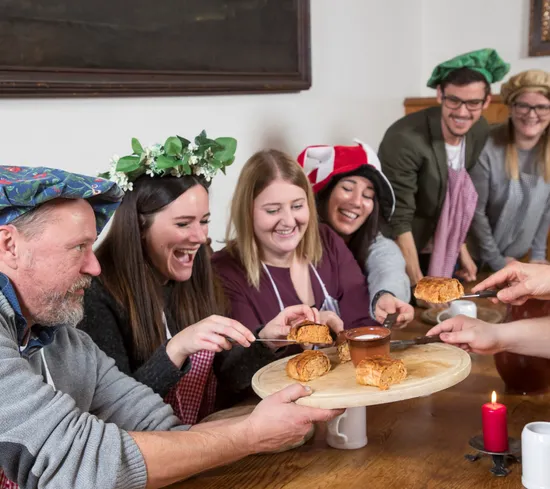 Group of people in medieval costumes sharing pastries and dipping sauce at a rustic table